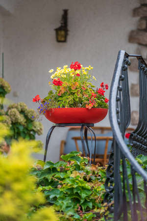 Beautiful decorative red flowerpot with flowers on the stairs in the house in the mountain village at summer day in Alps Austria, travel and nature conceptの写真素材