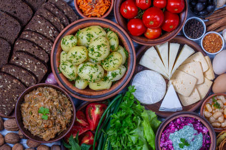 Assorted food: boiled young potatoes, beans, braised cabbage, beet salad with cottage cheese, sliced cheeses, pickled tomatoes, korean carrot, black bread with seeds, green lettuce leaves, spice, eggの写真素材