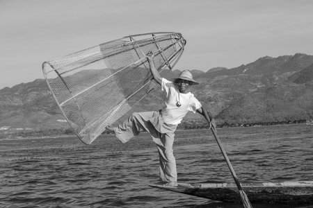 Inle lake, Myanmar - Jan 14, 2016: Burmese fisherman on bamboo boat catching fish in traditional way with handmade net. Inle lake, Myanmar, Burma, Black and whiteのeditorial素材