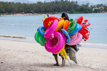 Island Mauritius - March 07, 2017: Beach seller of inflatable toys and swimming laps for tourists goes along the sand beach in island Mauritiusのeditorial素材