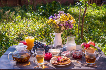 Black tea, pancakes, milk and jam on the breakfast table in the autumn garden, close up