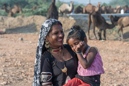 Pushkar, India - Nov 14, 2018 : Indian young woman with child in the desert Thar on time Pushkar Camel Mela near holy city Pushkar, Rajasthan, India, close up portraitのeditorial素材