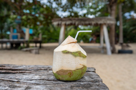 Sweet green coconut water with drinking straw on wooden table. Coconut tropical fruit on the beach...