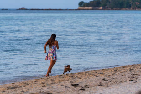 Koh Phangan, Thailand - Feb, 21, 2022 : Woman and dog running free on beach at sunset. Happy girl and her pet play out together on island Koh Phangan, Thailandのeditorial素材
