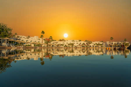 Buildings, sun loungers and parasols are reflected in the calm sea water on the beach in the resort town in the morning in Sharm El Sheikh during sunrise, Egyptのeditorial素材