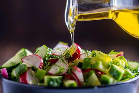 Pouring olive oil on healthy fresh vegetables salad, close up. Delicious vegetable diet salad of cucumber, radish, green onion, dill and olive oil. Concept healthy meal and mediterranean kitchenの写真素材