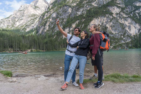 Lago di Braies, Italy - Aug 26, 2021 : Group of young tourists take pictures of themselves on a smartphone against the backdrop of lake Braies, Italyのeditorial素材
