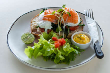 Toast with poached eggs, tomato and salmon on plate in cafe, close up, breakfast timeの写真素材