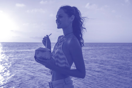 Young beauty girl drinking coconut at tropical beach near sea water at paradise island at sunset....