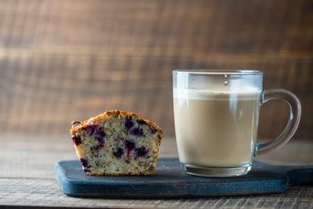 Delicious muffin with blueberries and cappuccino glass cup on a wooden table, close up. Fresh cupcake and coffee for breakfastの写真素材