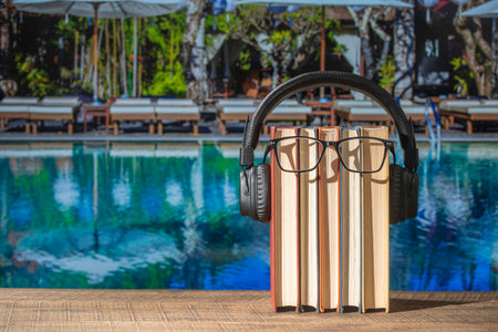 Set of books, headphones and eyeglasses on wooden table near swimming pool, close up. Audiobooks and education conceptの写真素材