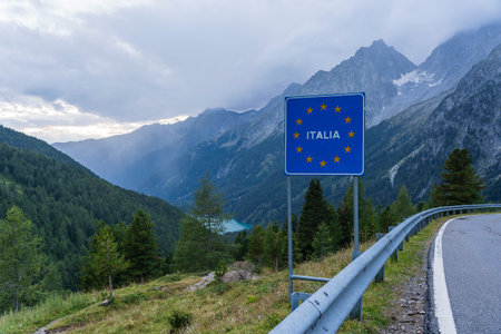 Road signal on the Italian border with many yellow stars of European Union and landscape of Hochgall mountain peaks covered by clouds, valley and Antholzer See lake in Dolomites, Italyの写真素材