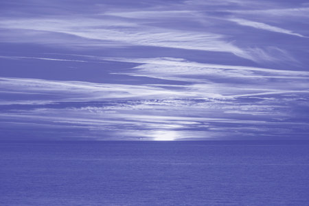 Majestic view of a setting down sunset sun with a sea water surface. Sunset sky with clouds and sea water. Trendy color of the year 2022. Ultra Violet creative and moody color of the pictureの写真素材