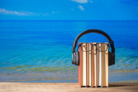 Set of books, headphones and eyeglasses on wooden table near sea water on the beach, close up. Audiobooks and education conceptの写真素材