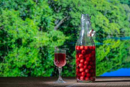 Homemade cherry brandy in a crystal glass and a glass bottle on a wooden table on nature background on a sunny summer day, close upの写真素材