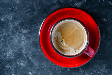 Red porcelain coffee cup with saucer over black background, top view, copy space, close up. Hot coffee in a breakfastの写真素材