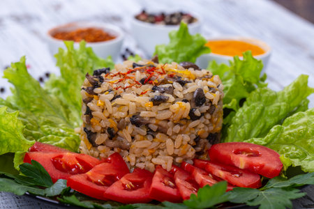 Rice with mushrooms, red tomato, onion, carrot and green lettuce leaves on rustic table background, close upの写真素材