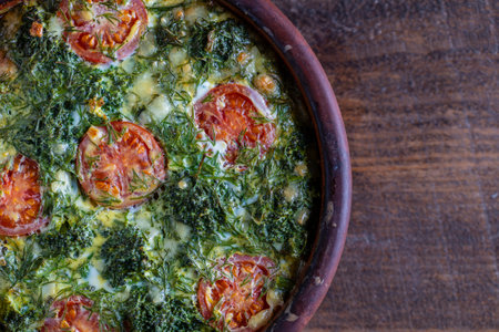Ceramic bowl with vegetable frittata, simple vegetarian food. Frittata with egg, tomato, pepper, onion, green broccoli and cheese on wooden table, close up, top view. Italian egg omeletteの写真素材