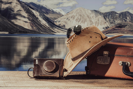 Vintage photo of suitcase, sun hat, photo camera and sunglasses with the Himalayan mountains background and blue water lake on a sunny day, close up. vacation and travel conceptの写真素材