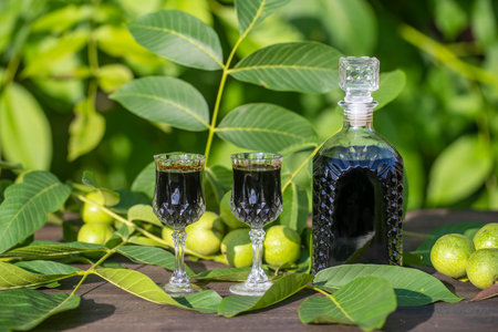 Liqueur from young green walnuts, remedy for stomach ache, close up. Tincture of green walnuts in a glass bottle on a table in the gardenの写真素材