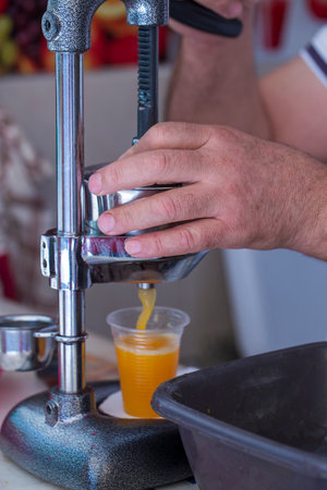 Man crushes juice from a fresh orange, close up. Cooking freshly squeezed orange juice with a...
