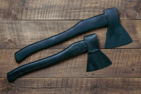 Two black axes on wooden background, top view, close up