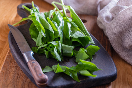 Ramson or wild garlic and knife on a cutting board on a wooden table, close up. Green leaves of wild garlic for salad preparationの写真素材