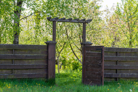 Wooden garden fence with open door and green grass on a spring day at backyardの写真素材