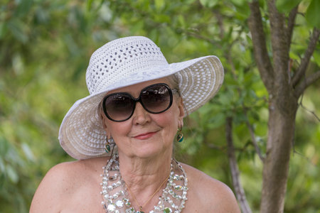 Portrait of a happy elderly woman 65 - 70 years old in a straw hat on the background of nature, close upの写真素材