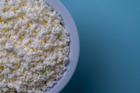 White cottage cheese in plate on blue background, top view, close up, copy space for text