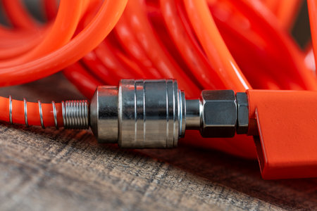 An orange air hose with an hose coupling on a wooden background, close up. Detail of air compressor...