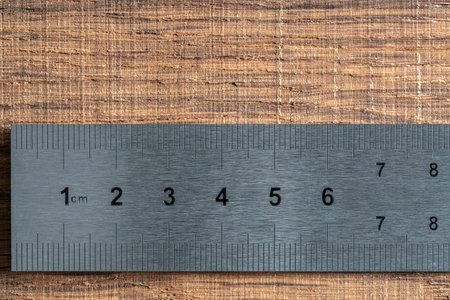 Fragment of an old metal ruler on wooden background, macro. Industrial steel ruler in centimeters, close upの写真素材