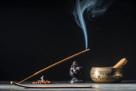 Asian incense stick in stick holder burning with smoke on black background, close up, copy space. Meditation, yoga, self development and sound therapy conceptの写真素材