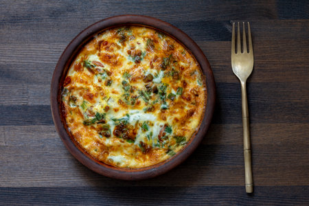 Ceramic bowl with vegetable frittata, simple food. Frittata with eggs, pepper, onion, greens and cheese on wooden table, close up, top view. Italian egg omeletteの写真素材