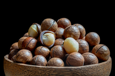 Macadamia nuts with shells in bowl on a black background, close up