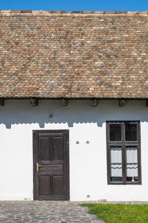 Detail of old rural house with tiled roof, window and wooden door in the ethnographic village of Holloko in Hungary, Europeの写真素材