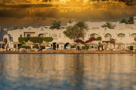 Buildings, sun loungers and parasols are reflected in the calm sea water on the beach in the resort town in the morning in Sharm El Sheikh during sunrise, Egyptの写真素材