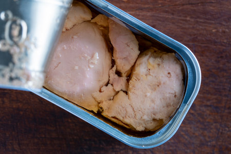 Open tin can with code liver on wooden table background, close up, top view