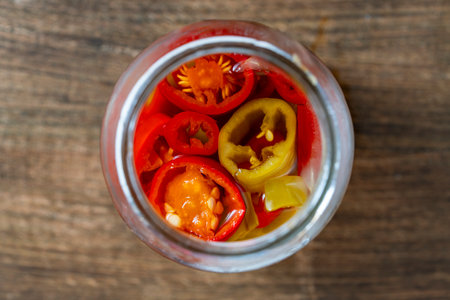 Pickle red and green chilli peppers with vinegar in glass jar on a wooden table, close up, top view