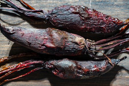 Three baked young beets in skins on a wooden cutting board, close up, top view. Organic vegetables,...