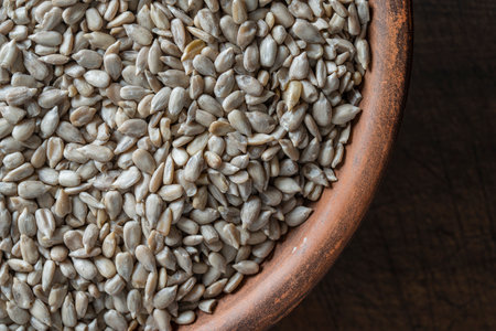 Gray raw sunflower seeds in ceramic bowl on a wooden background, close up, top view, copy space....