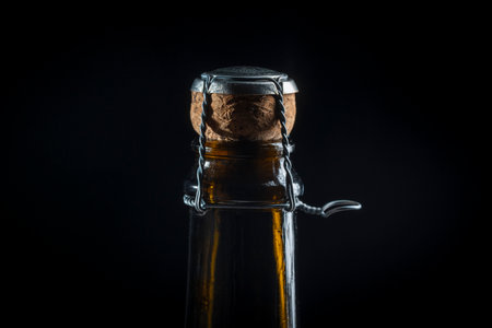 Close-up of a dark glass champagne bottle neck with cork and wire cage against a black background. Ready for a festive celebration. Macro photography of bottle sparkling wine and corkの写真素材