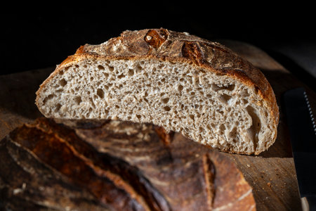 Half round loaf of freshly baked sourdough bread on wooden cutting board, close up. Rustic sourdough...