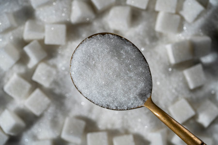 White granulated sugar in spoon in the background pile sugar cubes, top view, close up.