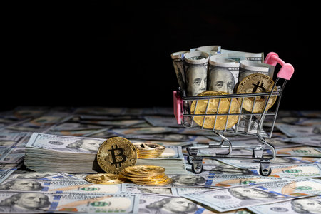 Cryptocurrency gold bitcoin coins and dollars in little shopping trolley on US 100 dollars bills background, close up. Digital money and bitcoin conceptの写真素材