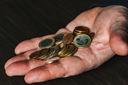 Old male hand holding euro coins, close up. Hands hold euro coins of different denominations. Inflation, purchasing power and social crisisの写真素材