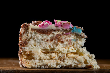 Piece of cake with chocolate cream and decorative top on black background, close up