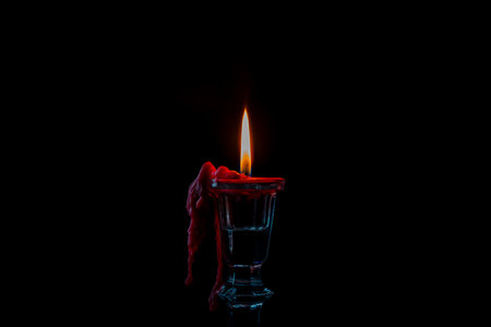 Glass candlestick with red burning candle on black background, close up