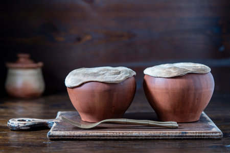Two clay pots on a wooden table, close up. Stewing food in earthenware is considered healthy