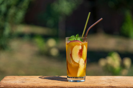 One glass of a summer cocktail or cold tea with peach slices, ice and mint on the nature background. Close up, copy spaceの写真素材